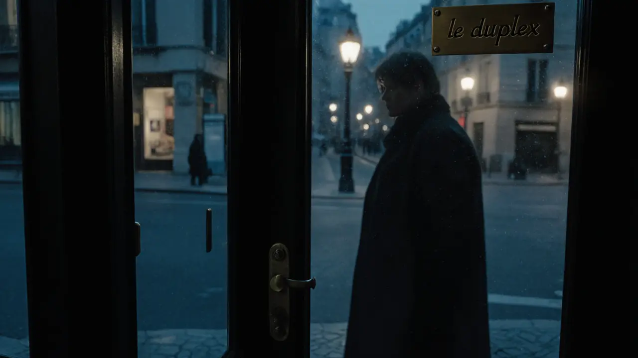 A plain black door with a small brass plaque in a quiet Parisian street at night.